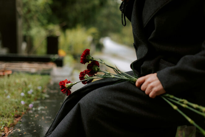 Person mit Rosen kniet am Grab (Bild: Kateryna Hliznitsova/Unsplash)